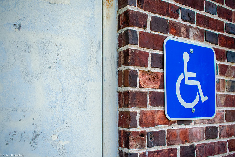 A blue sign with a white outline of a person in a wheelchair mounted on a red, brick wall.